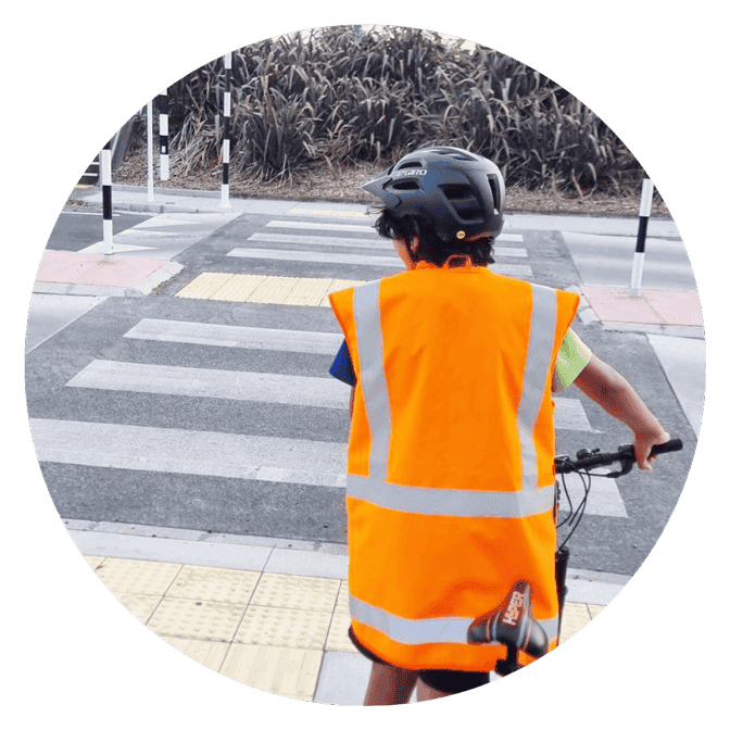 A boy on a bike waiting at a crossing, wearing a hi-vis vest.