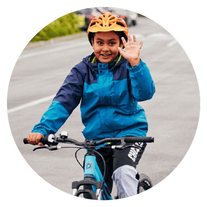A girl cycles towards the camera waving with one hand.